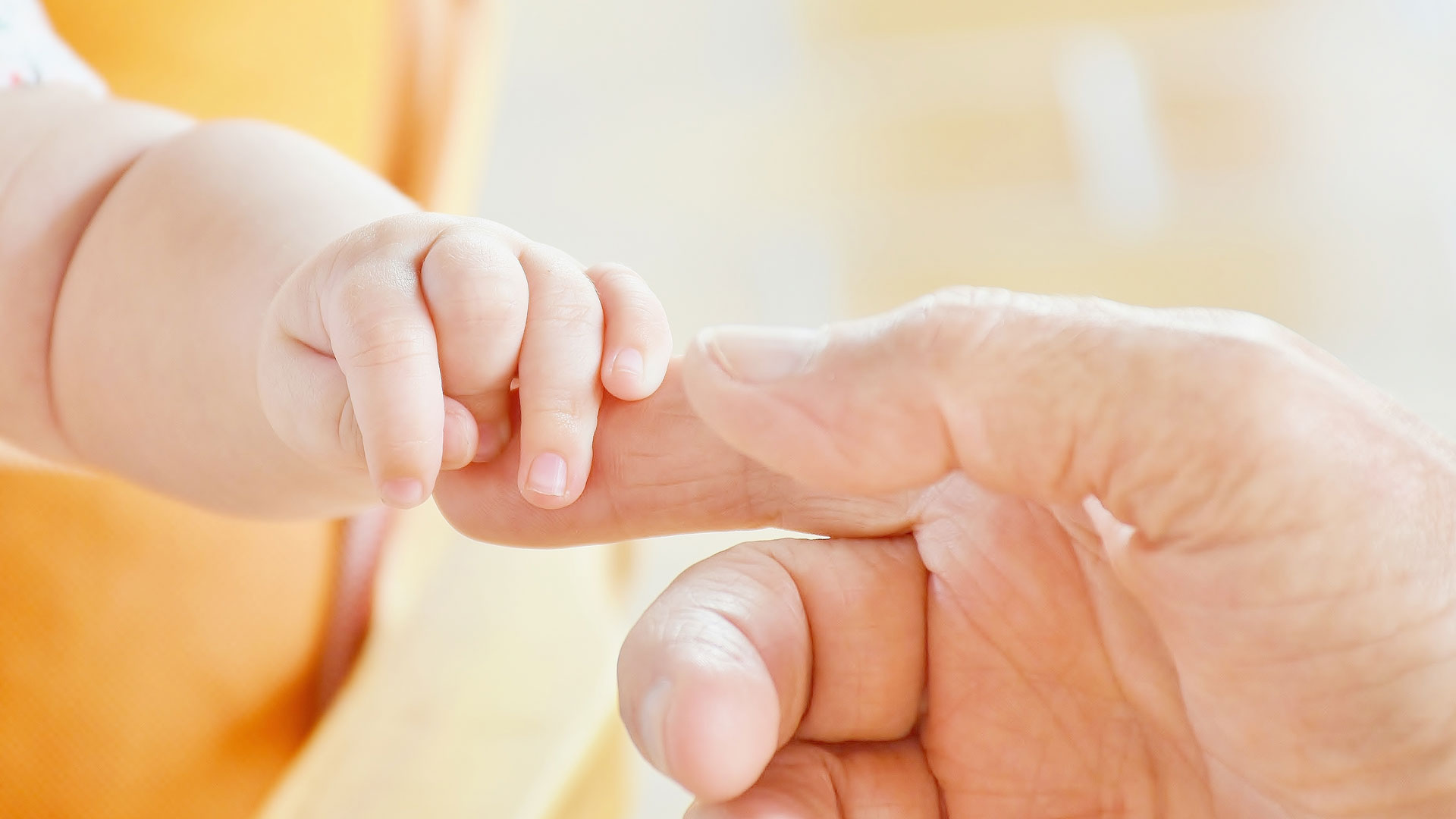 A baby's hand gripping an adult finger,