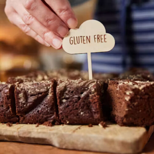 Shop or cafe assistant placing 'gluten free' label on chocolate brownies Daisy-Daisy/Getty