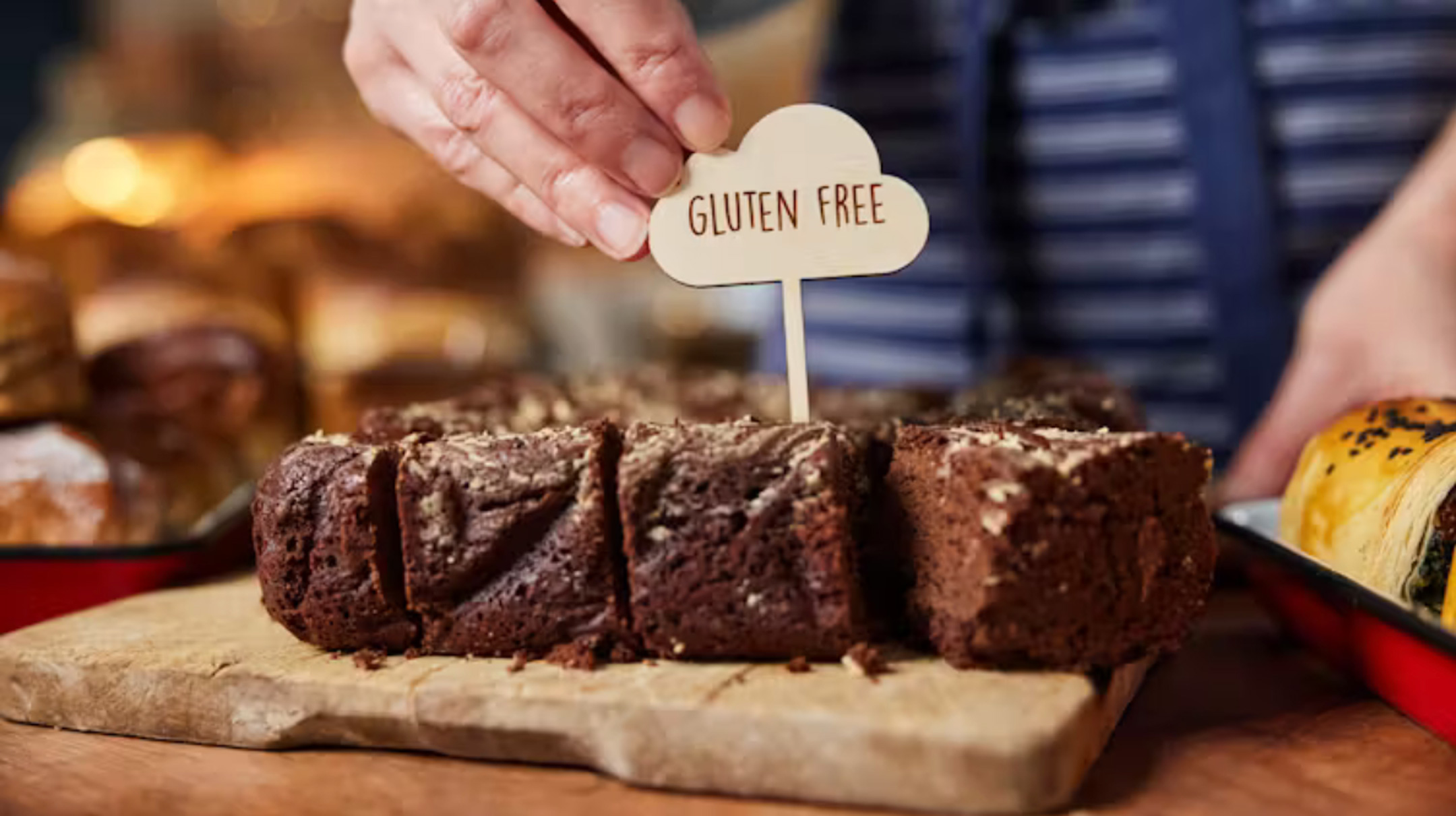 Shop or cafe assistant placing 'gluten free' label on chocolate brownies Daisy-Daisy/Getty