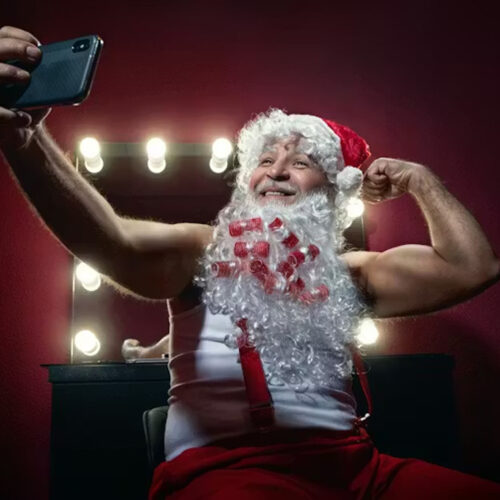 Narcissistic Santa Claus making selfie with mobile camera against the mirror. Wallenrock/Shutterstock
